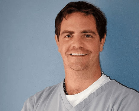 A man wearing scrubs and smiling at the camera.