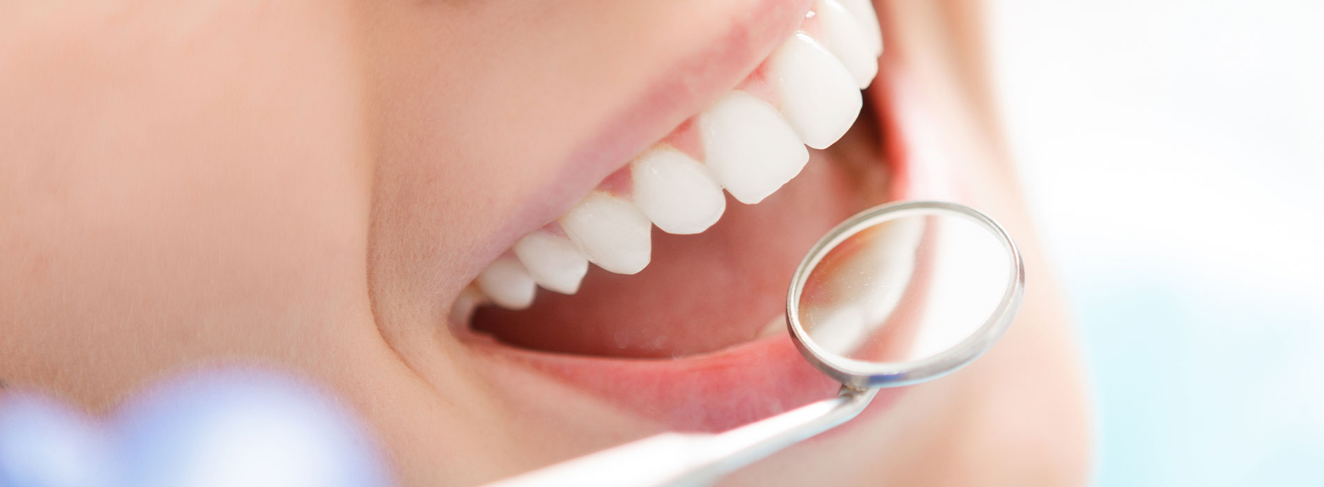 The image shows a person with a wide smile revealing white teeth, holding an object that appears to be a toothbrush or dental tool near their mouth, with a focus on cleanliness and dental care.