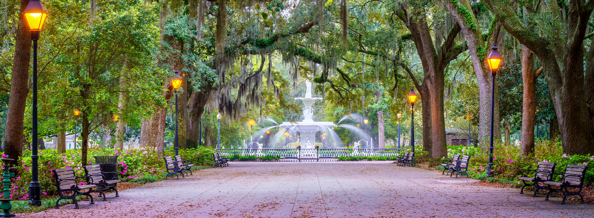 A large fountain at the end of a tree-lined park walkway.