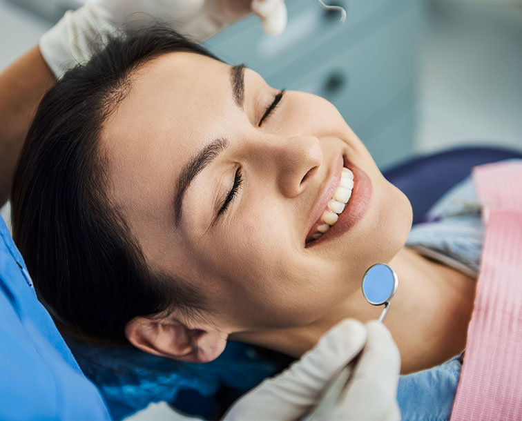 A woman in a dental office receiving dental care, smiling with eyes closed.