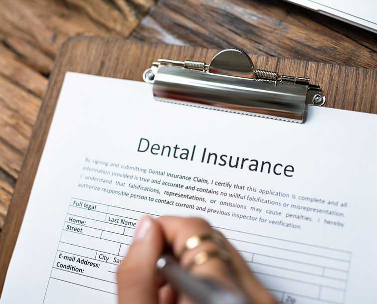 The image shows a person writing on a clipboard with a pen, which has a form titled  Dental Insurance  displayed prominently.