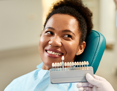 A smiling woman sitting in a dental chair with a tray of dental tools in front of her.