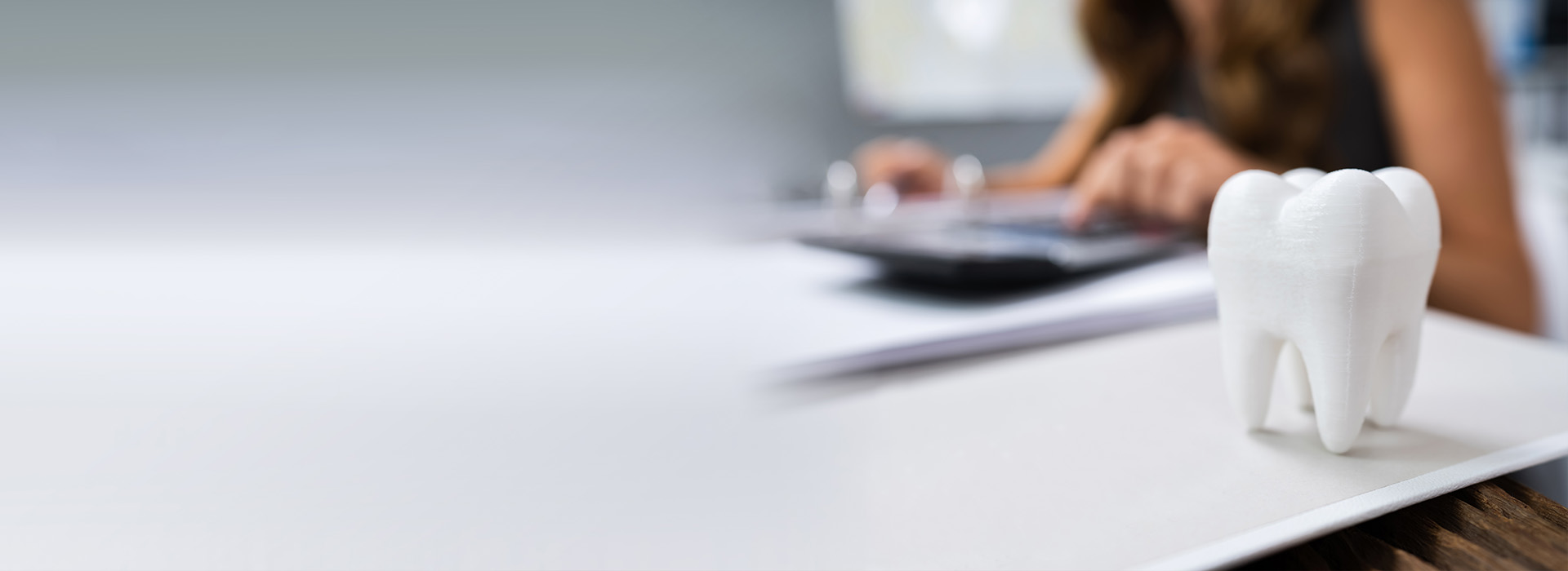 The image shows a person working at a desk with a computer mouse and keyboard, and there s a playful element of a tooth-shaped object resembling a building.