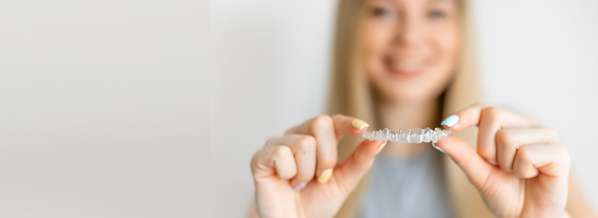 A smiling woman holding up a ring with her right hand against a white background.