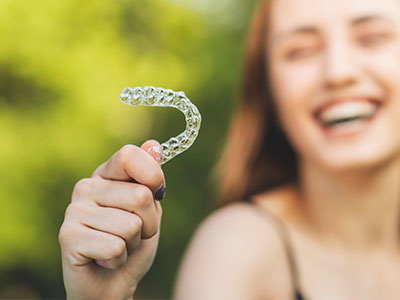 A smiling woman holding up a toothbrush with a bristle-like structure, possibly for dental use or demonstration.