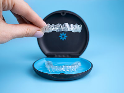 An image showing a person s hand holding an open box containing a set of transparent dental aligners.