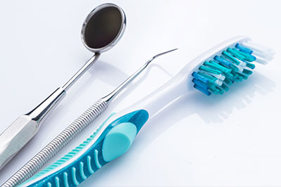 The image shows dental instruments including a toothbrush with blue bristles, placed next to a pair of metal tweezers on a white background.