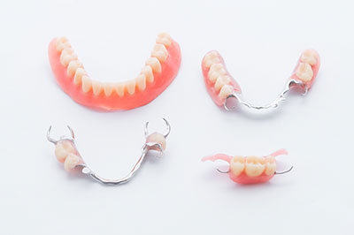 The image shows three pairs of dentures with teeth in various states of wear, displayed on a white surface against a neutral background.