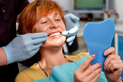 A woman sitting in a dental chair with her mouth open, receiving dental care, while holding a blue dental impression tray.