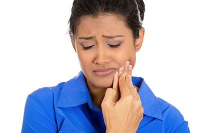 A woman with her eyes closed, holding her face with both hands, seemingly distressed or in pain.