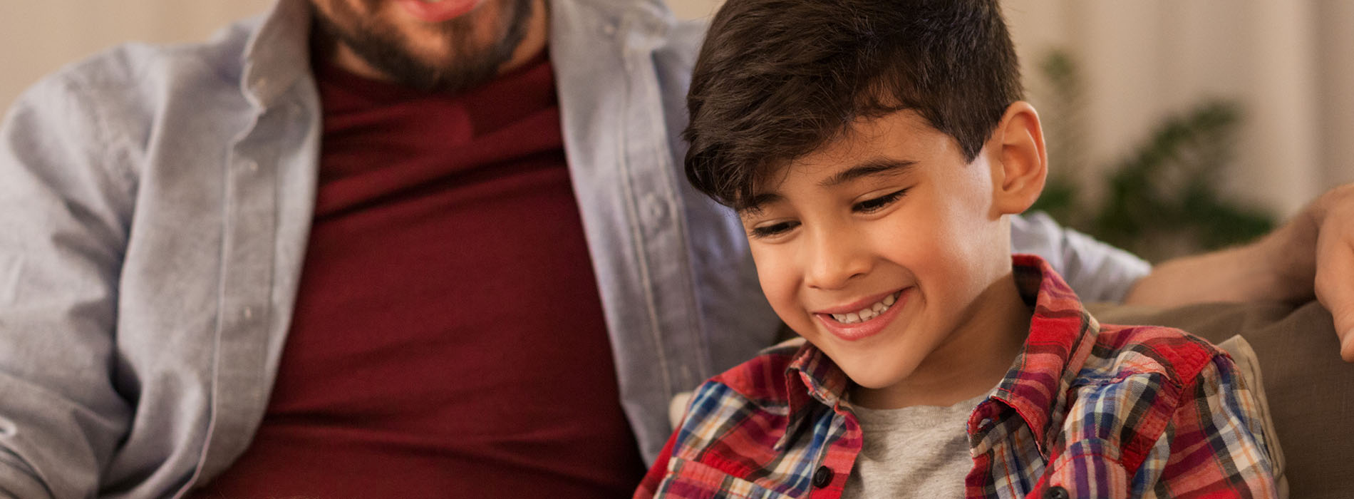 A man and a young boy are smiling at each other with their arms around each other  they appear to be sharing a happy moment together.