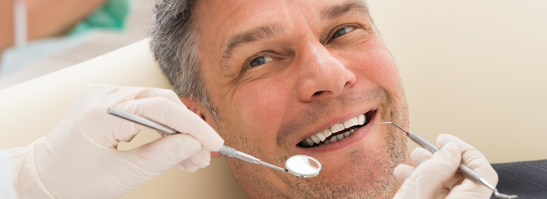 The image shows a man sitting in a dental chair with his mouth open, receiving dental treatment from a dentist who is working on him.