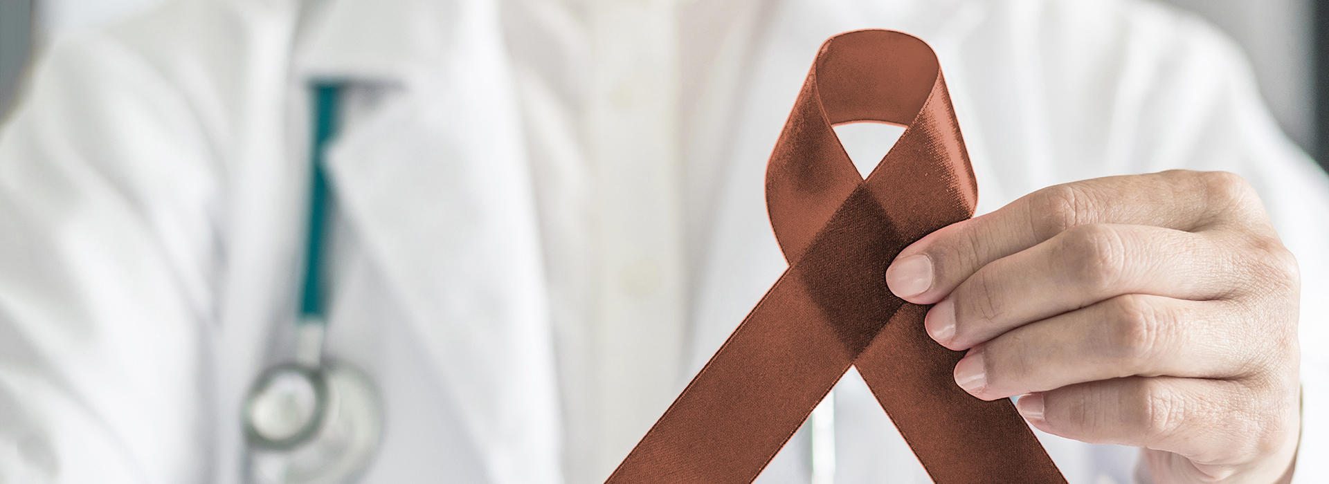 The image shows a person holding up a red ribbon with a white cross symbolizing medical aid, indicating a connection between healthcare and cancer awareness.