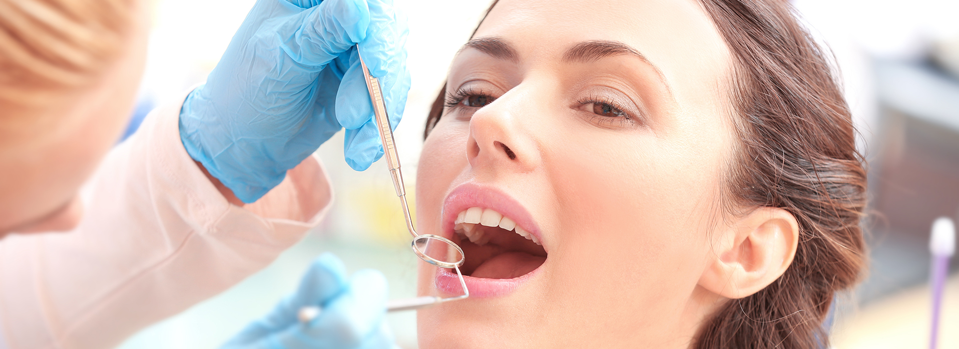 The image depicts a woman receiving dental treatment, with a dentist performing a procedure on her teeth while she wears a protective mouthguard.