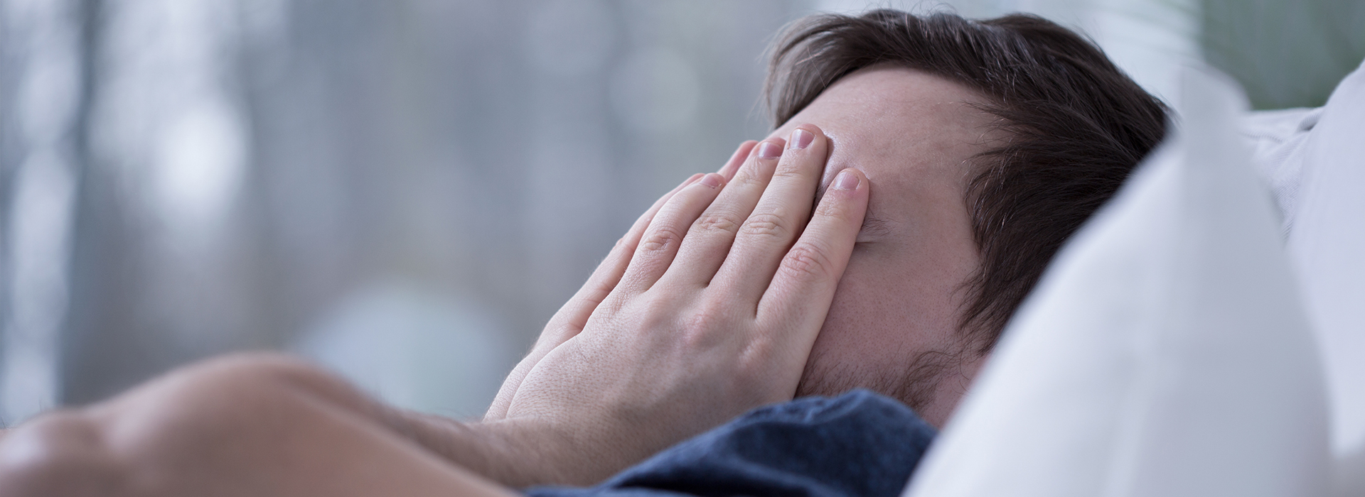 A person lying on their stomach with their head turned away from the camera, covering their face with their hands.