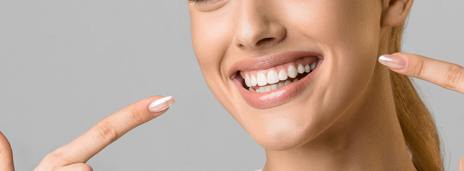 A woman with a radiant smile, holding up two fingers on her face, against a white background.