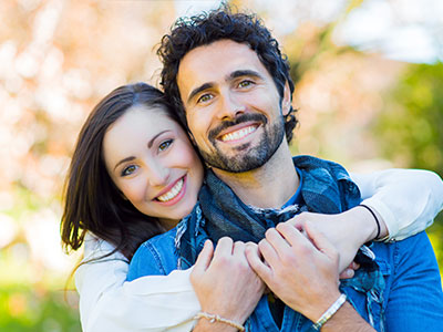 A man and woman are hugging each other warmly outdoors during daylight.