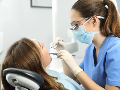 The image shows a dental hygienist performing a dental procedure on a patient in a dental office setting.