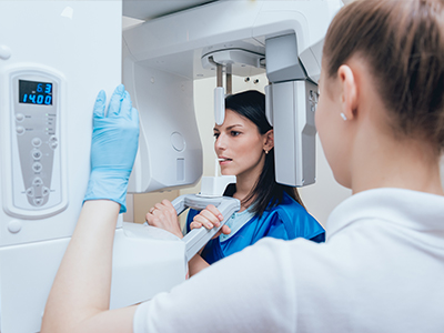 A medical professional stands beside a large, modern MRI machine, assisting a patient who is lying on the scanner bed.