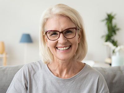 A woman with short hair wearing glasses, smiling slightly at the camera. She has blonde hair and is dressed in a casual top.