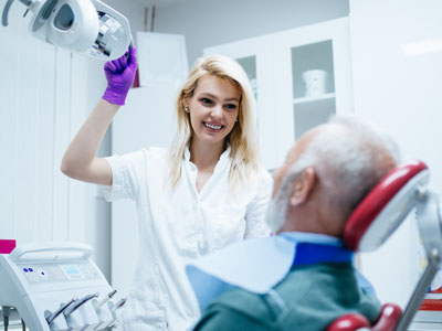 A dentist in a white coat assisting an older patient with dental equipment.