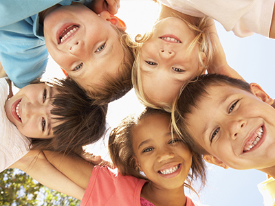 The image depicts a group of children posing together with smiles, under a clear sky.