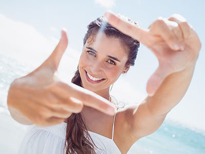 Woman holding up peace sign against blue sky background.