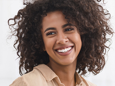 A woman with curly hair and a smile, wearing a light-colored top, against a white background.