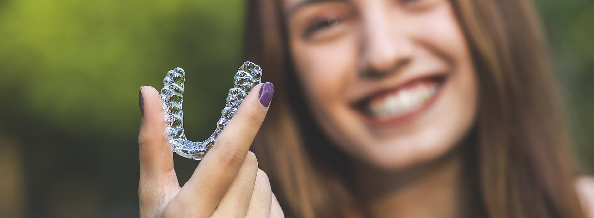 The image features a person holding up a clear plastic aligner tray with a smile, suggesting dental alignment treatment.